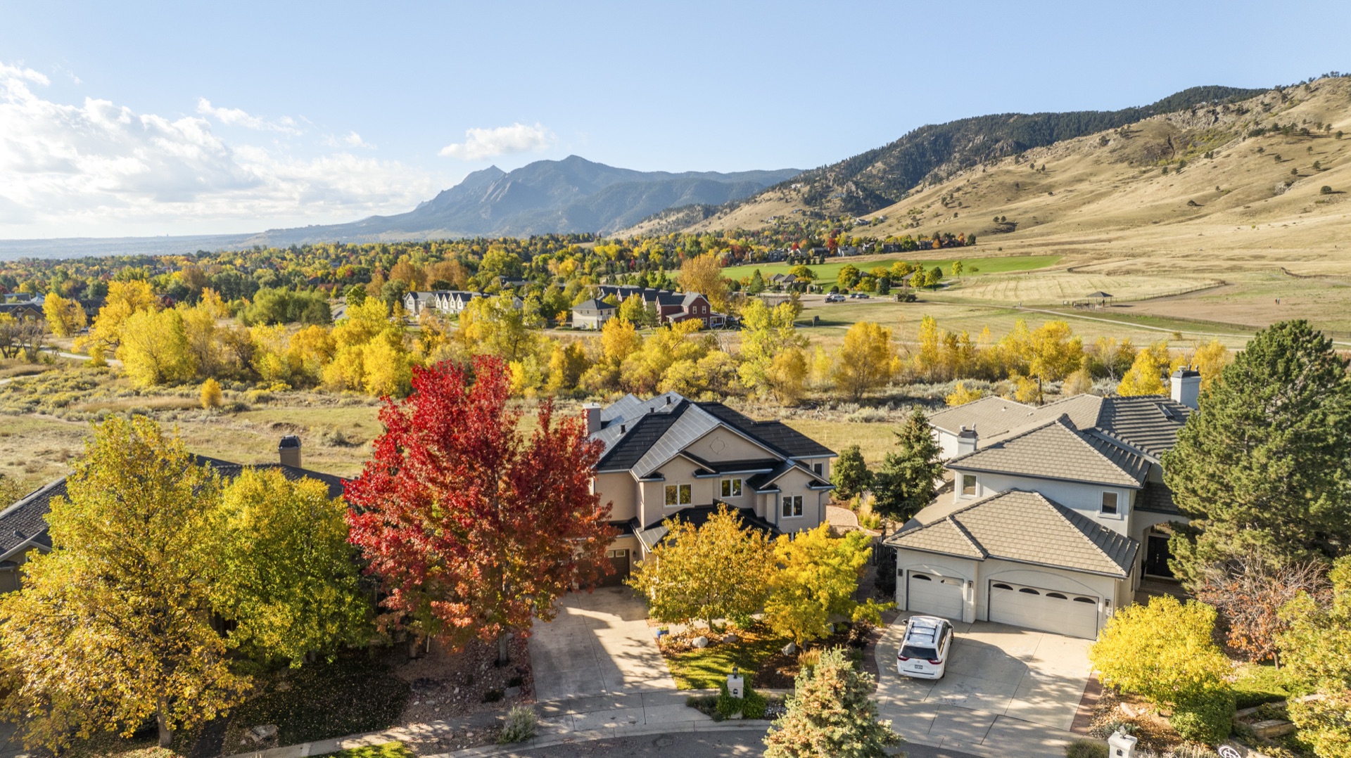 Aerial view of a Boulder neighborhood in fall color with the Flatirons and blue sky